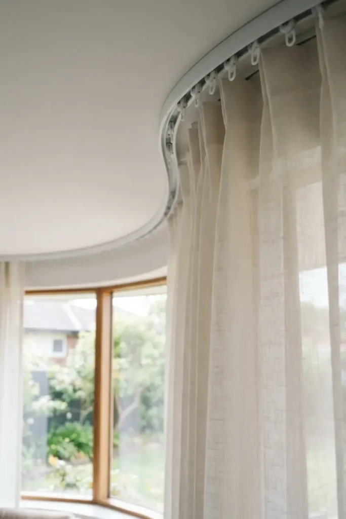 Curved curtain track hidden along ceiling with linen curtains in bay window