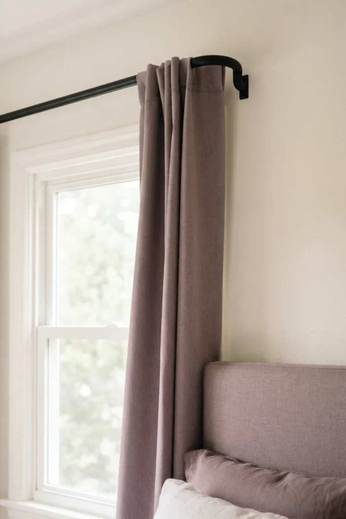 Bedroom blackout curtains in dusty mauve on a matte black wraparound rod so the fabric meets the wall with no side gap