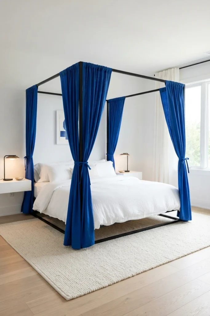 Canopy bed curtain ideas featuring a bold cobalt blue canopy on a black four-poster frame in an all-white bedroom