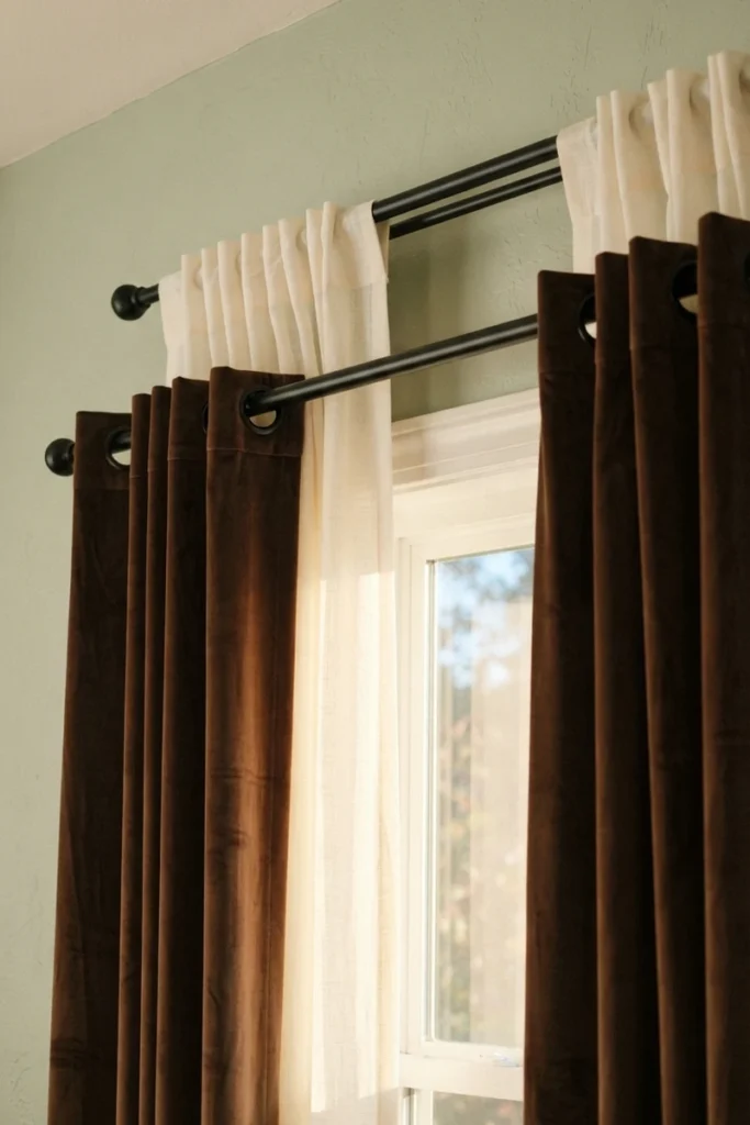 Layered curtains for living rooms combining an ivory back-tab sheer with chocolate brown velvet grommet drapes on a black double rod