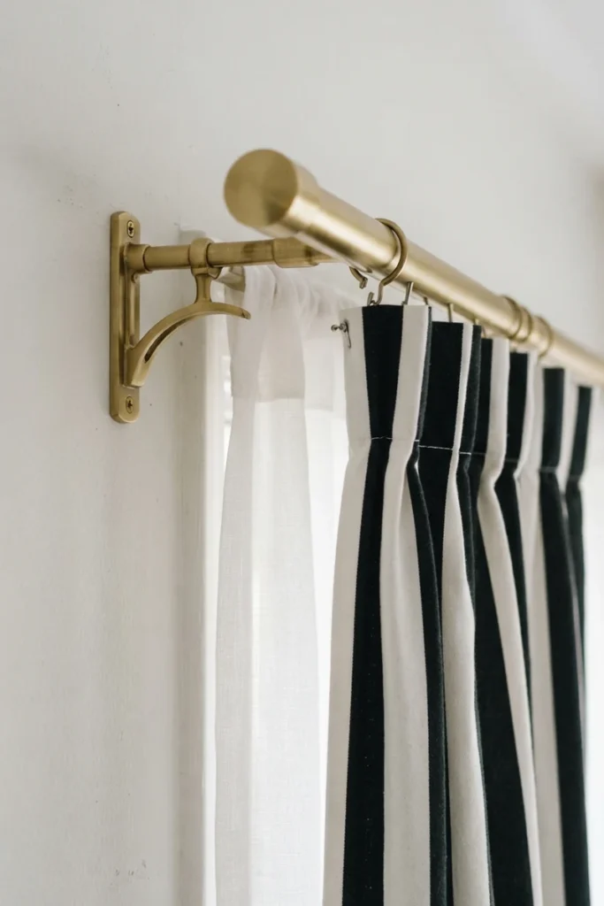 Layered curtains for living rooms on a brass double rod bracket showing black and white striped drapes projecting in front of a white sheer